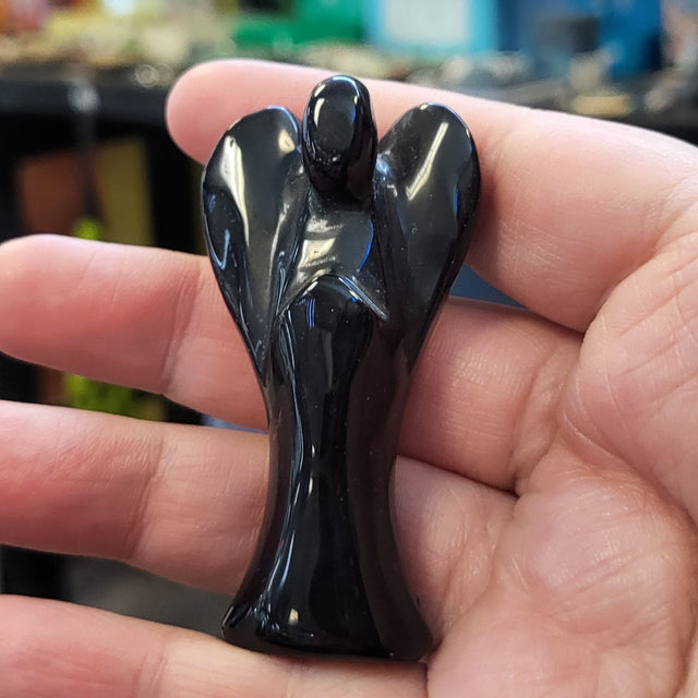 Hand holding a black obsidian angel with a blurred store background