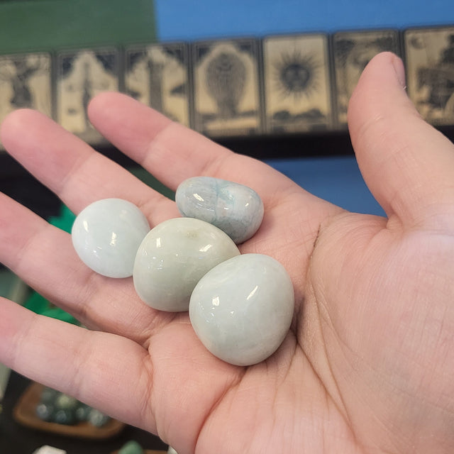 Hand holding three light green jade stones with a blurred background