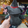 Plush crow doll named "Ascrowdeus", viewed from the back. Doll is overall black. It has plush wings and tail with embroidered detail, all of which is black. It also has a black witch's hat with red hat band.