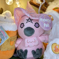 Plush crow doll named "Alice Crow-ley", viewed from the front. Doll is overall pink except for violet embroidered eyes, grey plush beak and feet, and black embroidered details for pentagram and eyeliner. It has pink plush wings and feather beard with embroidered pink detail. It also has a pink witch's hat with white star print with a violet hat band.