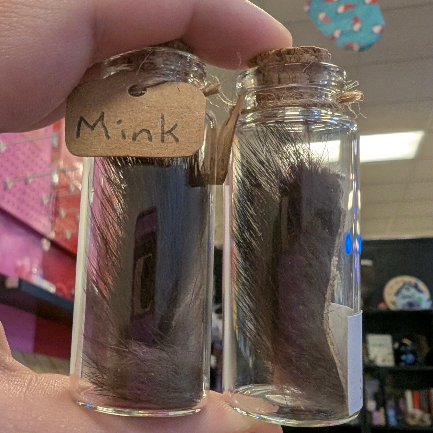 Two glass jars with fur samples labeled 'Mink' held by a hand.