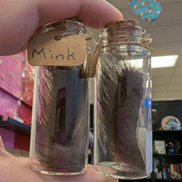 Two glass jars with fur samples labeled 'Mink' held by a hand.