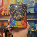 Hand holding a colorful box with text in front of a shelf with various items.