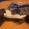A dark brown and black fur pelt with a natural bear jawbone with crystal teeth lying on top, displayed on a wooden table against a dark blue wall.
