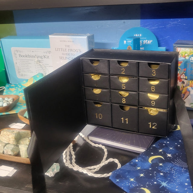 Black advent calendar with gold numbers on a blue surface with tarot card designs.