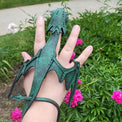 Green dragon-shaped sandal on a hand with a garden background