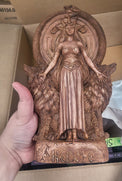 Hand holding a detailed wooden sculpture against a cardboard box background
