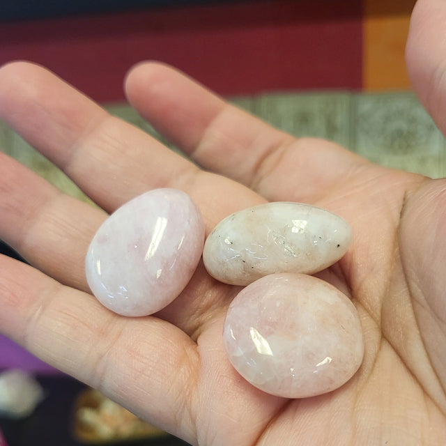 Hand holding three pink stones with a blurred background