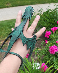 Green dragon scale glove held by a hand with a garden background