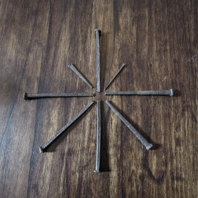 Blacksmith-made nails in different sizes arranged into a star pattern on a wood background